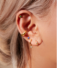 Close up a model's ear wearing gold earrings featuring a mix of semi-precious gemstones.