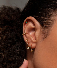 Close up of a model's ear, wearing a mix of gold earrings including some gemstone huggies.