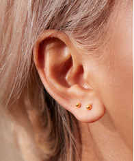 Close up of a model's ear, wearring two gold piercing stud earrings.